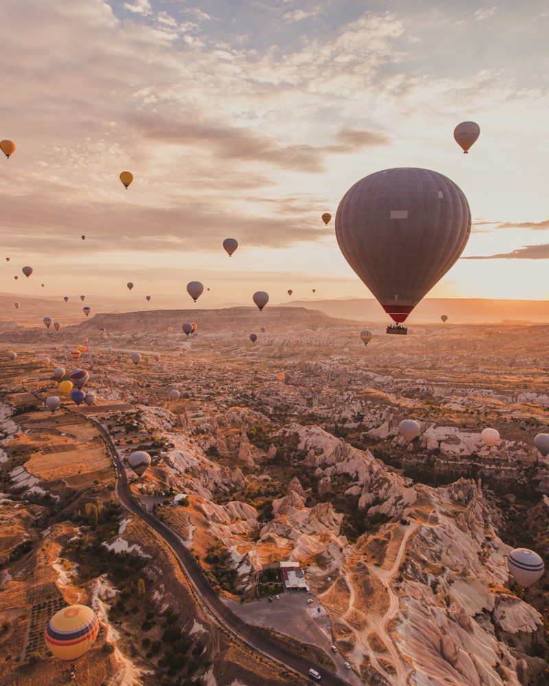 travel and inspiration, hot air ballons in Turkey flying at sunrise sky Smiling woman looking at her phone while using laptop to book a trip
